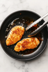 This image shows breaded chicken sizzling in a pan, turning golden brown and crispy as it cooks to perfection.