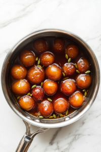 This image shows the Gulab Jamuns absorbing the sugar syrup, becoming soft, juicy, and infused with rich sweetness.