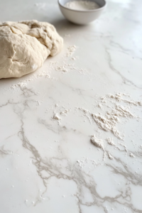 This image shows hands kneading the dough, working it into a smooth and elastic texture, essential for achieving a soft and fluffy loaf of Amish bread.