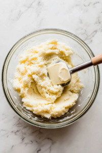 This image shows a potato masher pressing into a pot of cooked potatoes, creating a smooth and creamy consistency that will thicken and enrich the Shepherd’s Pie Soup.