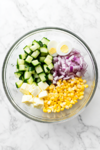 This image shows a large mixing bowl filled with freshly chopped crab meat, diced onions, zucchini, and boiled eggs, ready to be combined for the first step in making Russian Crab Salad.