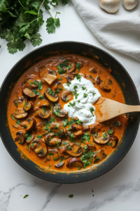 This image shows fresh mushrooms being added to the rich curry base along with whisked yogurt, ensuring a creamy and well-balanced Mushroom Masala.