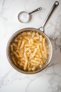 This image shows pasta boiling in a large pot of water, cooking until perfectly tender and ready to be combined with fresh ingredients for a delicious crab pasta salad.