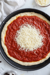 This image shows the dough being pressed evenly across the pizza pan, forming a slight edge to hold the pizza toppings.