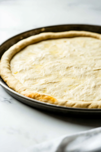 This image shows the pizza dough being punched down to release air, and the pizza pan is brushed with oil in preparation for shaping the dough.