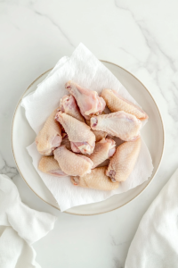 Raw-chicken-wings-being-patted-dry-on-a-cutting-board-before-seasoning-and-baking-3824833-683x1024-9708588
