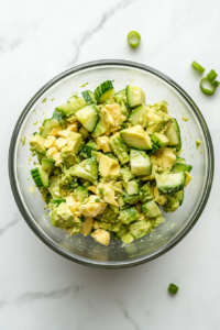 This image shows the completed cucumber avocado salad, served immediately in a glass bowl, looking fresh and vibrant with a burst of green and citrusy flavors.