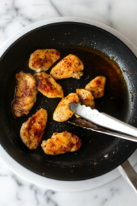 This image shows cooked chicken being removed from the skillet and placed on a plate, ready for the next step.