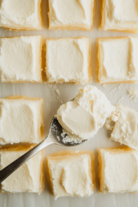 This image shows a spoonful of smooth cream cheese filling being placed in the center of each puff pastry square, ready for folding.