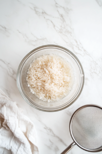This image shows basmati rice being rinsed under clean water and soaked to enhance its texture, ensuring each grain remains fluffy, long, and perfectly cooked in the Chicken Dum Biryani.