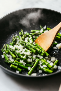 This image shows onions and asparagus being sautéed in a skillet until tender and fragrant.