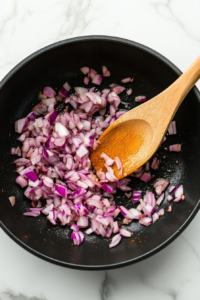 This image shows finely chopped onions being sautéed until golden brown, enhancing the depth and sweetness of the Goan Fish Curry.