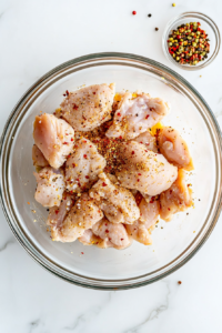 This image shows raw chicken being seasoned with spices on a cutting board, preparing it for cooking.