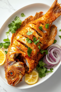 This image shows a beautifully plated whole fried fish, crispy and golden, with onion rings and a lemon wedge on the side for a perfect finishing touch.