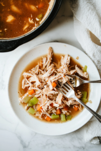 This image shows tender shredded chicken being returned to the simmering pot of broth, bringing a hearty and comforting texture to the homemade chicken and noodles.