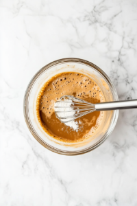 This image shows dry ingredients, including flour, baking soda, and warm spices, being sifted into the wet banana mixture, ensuring a light and even texture in the banana bread batter.