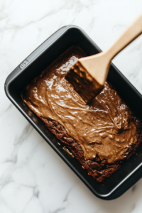 This image shows a stream of smooth banana bread batter being poured into a greased loaf pan, ensuring even distribution for a perfectly baked bread.