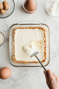 spreading-cream-cheese-mixture-evenly-over-cooled-crust-in-baking-dish