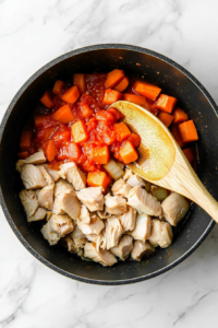 This image shows a spoon stirring minced garlic and vibrant tomato paste into a pan filled with sautéed ground turkey, onions, and carrots, enhancing the deep and savory flavor of the Shepherd’s Pie Soup.