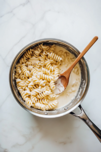 stirring-warm-rotini-pasta-into-the-rich-creamy-cheese-sauce-until-fully-coated