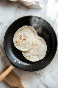 This image shows soft tortillas being toasted until lightly golden, making them warm and pliable for assembling tacos.