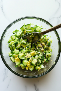 This image shows a hand gently tossing the cucumber avocado salad to ensure the lime juice, olive oil, and seasonings coat each ingredient perfectly for a balanced taste.