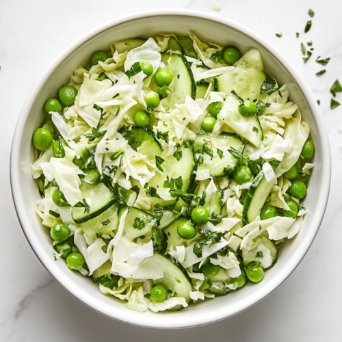 This image shows a vibrant cucumber pea salad in a white round bowl with chopped cabbage and peas, showcasing a fresh and green appearance.