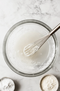 A small bowl of cornstarch and water being whisked together to create a smooth thickening agent.