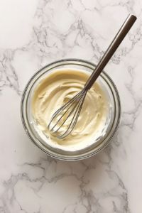 This image shows fresh yogurt being whisked into a smooth, lump-free consistency, ensuring it blends seamlessly into the curry without curdling.
