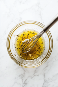 This image shows a hand whisking a tangy dressing in a small mixing bowl, preparing to add it to the cucumber feta salad for enhanced flavor.