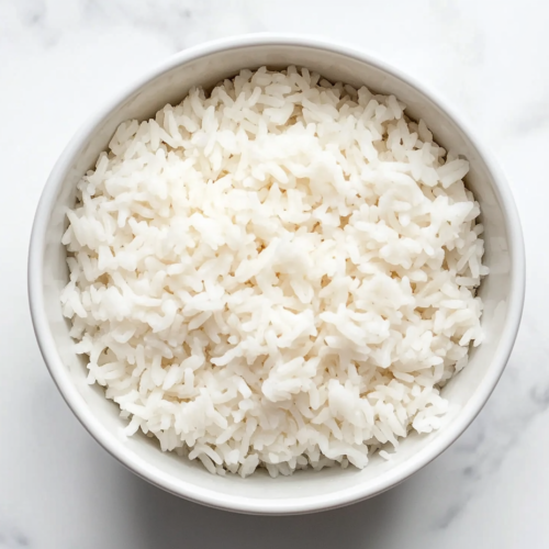 This image shows a bowl of freshly cooked white rice, perfectly separated and soft, served in a round white bowl, ready to be enjoyed.