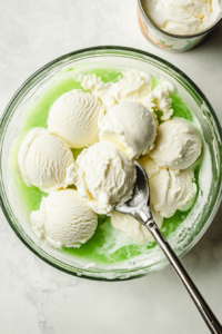 This image shows a generous scoop of vanilla ice cream being placed on top of the green Potion Punch. As it melts, it creates a creamy, frothy texture, enhancing both flavor and presentation.