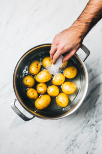 This image shows freshly chopped potatoes being added to a large pot, preparing them for boiling to make a soft and fluffy potato salad.