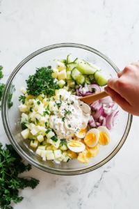 adding-hard-boiled-eggs-and-fresh-herbs-to-potato-salad