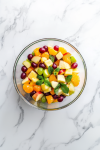 This image shows freshly sliced bananas being added to the chilled fruit salad just before serving. Their creamy texture and mild sweetness complete the refreshing dish.