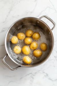 This image shows potatoes simmering in a pot of boiling water, cooking until they become tender and ready for the next step in making potato salad.