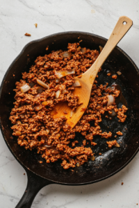 This image shows ground beef sizzling in a skillet as it browns. The beef is being cooked until it's no longer pink, ensuring a flavorful base for the casserole.