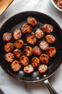 This image shows sausage being browned in a pan, forming a crispy and flavorful base for the Cajun rice dish