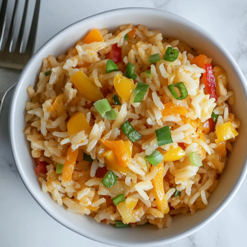 A vibrant bowl of Cajun rice, filled with rice, colorful veggies, and topped with freshly chopped green onions. A spoon rests in the dish, ready to serve this flavorful and aromatic meal.