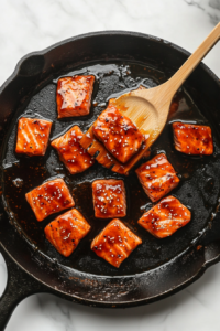This image shows the salmon bites cooking in the thickened honey garlic glaze, intensifying their rich and savory taste.