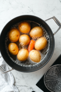 This image shows whole carrots and eggs being added to the boiling pot alongside potatoes, ensuring even cooking for a well-balanced salad.