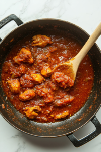 This image shows marinated chicken sizzling in the pan, its surface caramelizing as it absorbs the bold flavors of the masala. The chicken takes on a deep golden-red hue, promising a flavorful dish.
