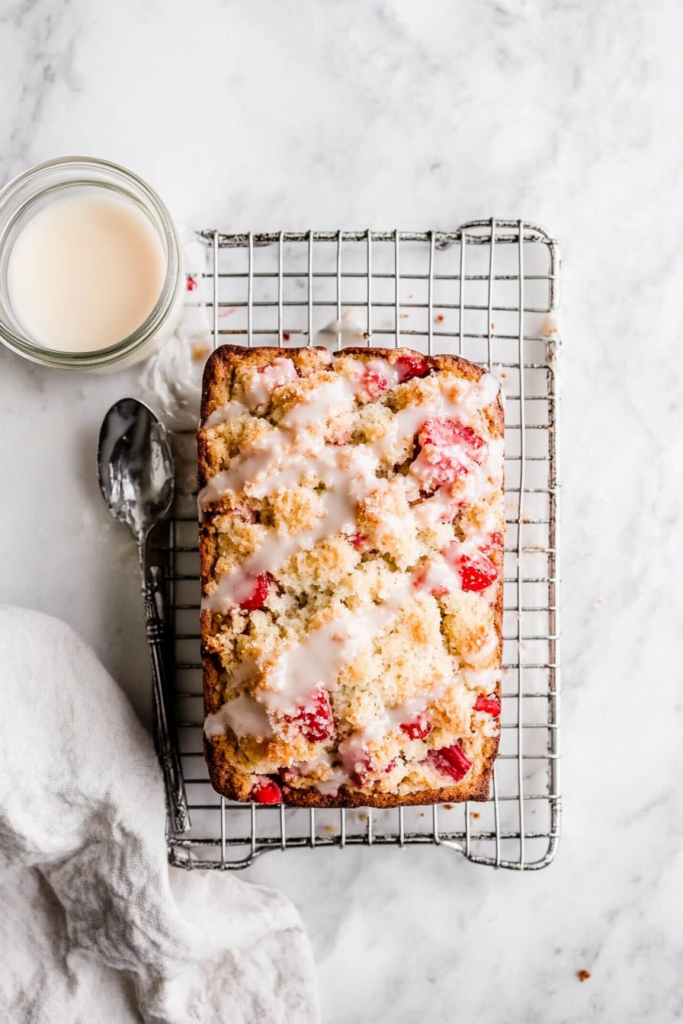 This image shows a smooth glaze being drizzled over the fully cooled strawberry rhubarb bread, adding the perfect finishing touch.