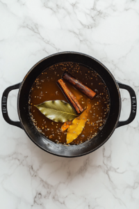 This image shows mustard oil shimmering in a pan, with whole spices like bay leaves, cinnamon, and black cardamom sizzling. Their fragrance fills the air, creating the base for an aromatic Chicken Karahi.