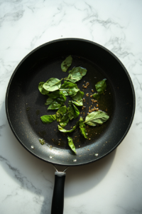 This image shows a pan with hot oil shimmering as whole spices like mustard seeds, fenugreek, and dried red chilies sizzle and crackle. The spices release their aromatic oils, creating the flavorful base of the Kerala Fish Curry.