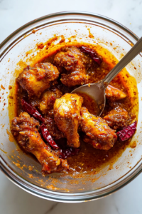 This image shows raw chicken coated in a deep red marinade of yogurt, chili powder, turmeric, and other bold spices. The chicken is absorbing the flavors, ensuring a juicy and aromatic bite after cooking.