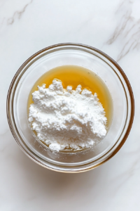 This image shows cornstarch being whisked into a bowl of broth, creating a smooth mixture to thicken the soup.