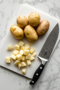 This image shows peeled and diced potatoes on a cutting board, cut into bite-sized pieces for a well-balanced potato salad.