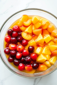 This image shows canned fruit cocktail being poured into a large mixing bowl, creating a sweet and juicy base for the refreshing fruit salad. The syrup coats the fruit pieces, adding a natural sweetness.