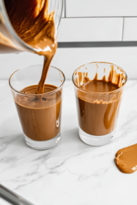 pouring-freshly-blended-chocolate-peanut-butter-smoothie-into-glasses-top-down-view
